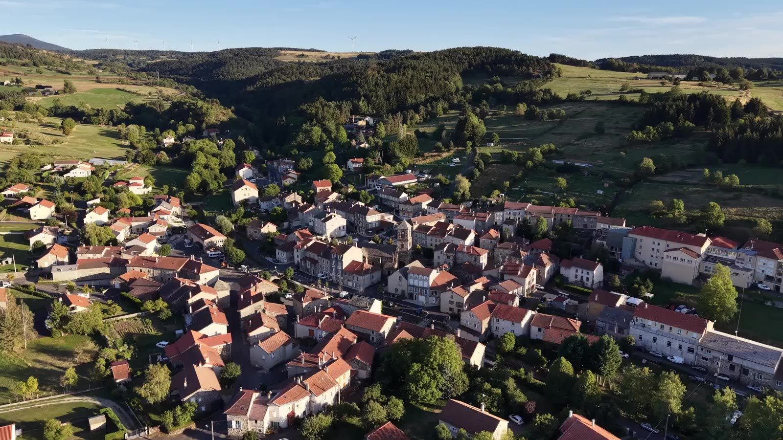 Vue aérienne du bourg de Laussonne : toits de tuiles, clocher de l'église Saint-Pierre et collines boisées